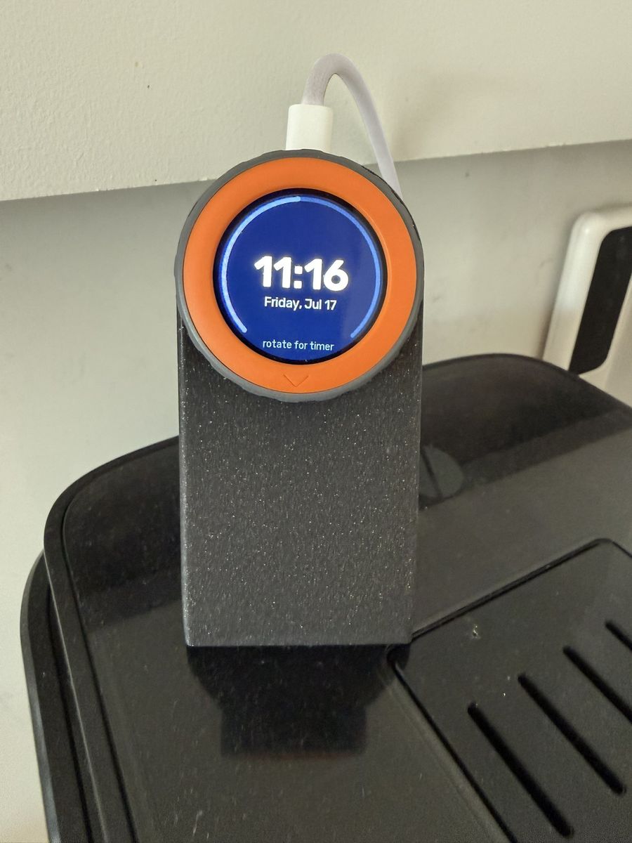 M5Stack Dial on a 3D-printed stand on top of a coffee machine, idle clock page showing 11:16, Friday Jul 17